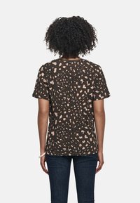 Das braun gemusterte T-Shirt hat ein Leopardenmuster mit beigen Akzenten. Es hat kurze Ärmel und einen lässigen Schnitt. Aus weichem Stoff, im Freizeitstil.