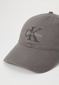 Grijze katoenen baseballpet met geborduurde "Calvin Klein" tekst en logo in contrasterende kleuren, gestructureerde kroon en gebogen klep.