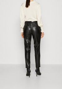 Svarta läderbyxor med slim fit, med hög midja och två bakfickor. Matcher med en krämfärgad tröja.