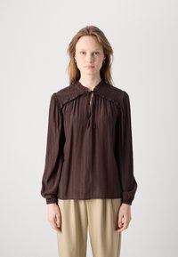 Brun bluse med smock-detajler på skuldrene, lange ærmer og knaplukning foran. Blød tekstur, letvægtsstof.