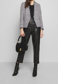 Blazer in tweed con bordi sfrangiati, top nero, pantaloni in pelle a vita alta e borsa a tracolla nera. Design texturizzato, con fantasia e aderente.