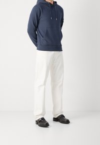 Felpa con cappuccio blu navy con tasca frontale, abbinata a pantaloni dritti color crema e scarpe in pelle nera con dettaglio a fibbia.