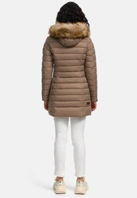 Hnědý péřový kabát s umělým kožíškem na kapuci, prošívaný design, střední délka. Nesený přes bílé kalhoty a béžové tenisky, pohled ze zadu.