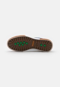 Semelle extérieure de chaussure de sport avec une base en caoutchouc marron, des éléments de traction verts et un logo Timberland ; présente un motif texturé pour l'adhérence.