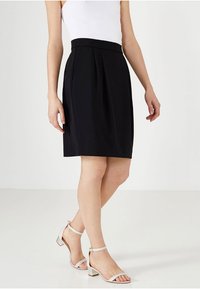 Černá sukně do áčka s plisováním v pase, vyrobená z hladké látky. Kombinována s světle zbarvenými sandály na podpatku se ramínky. Jednoduchý design, délka ke kolenům.