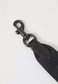 Schwarzer Nylonriemen mit einem metallischen Clip, ausgestattet mit einem runden Ring und Lederakzenten. Strukturierte Oberfläche mit Nähdetails.