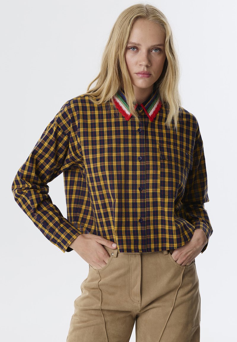 Camicia a quadri gialla e blu navy con colletto all'uncinetto che presenta strisce rosse, verdi e bianche. Parte anteriore con bottoni, maniche lunghe e vestibilità rilassata.