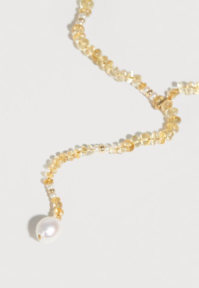 Collier délicat avec de petites perles translucides jaunes et un pendentif unique en perle blanche sur un fond clair.