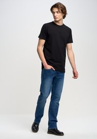 Camiseta de algodón negra, estilo cuello redondo, combinada con vaqueros azules. El modelo lleva botas de cuero negras. Conjunto simple y casual sobre un fondo claro.