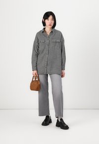 Black and white checkered oversized shirt with two chest pockets, paired with light gray straight-leg jeans and black platform shoes. Brown handbag.