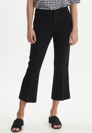 Pantaloni neri a croppati con una leggera svasatura, caratterizzati da una texture morbida e una vestibilità sartoriale. Abbinati a mule nere con punte aperte.