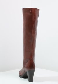 Bota marrón de cuero hasta la rodilla con tacón cónico. Textura suave, costuras mínimas y un logotipo grabado cerca de la parte superior. Diseño clásico.