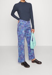 Haut à manches longues côtelé bleu marine associé à un pantalon bleu à motifs colorés et des sabots noirs. Accessoires comprenant un sac à main vert menthe.