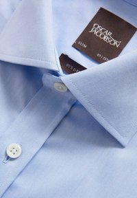 Lichtblauw, slim-fit overhemd met puntkraag. Heeft een gladde textuur, witte knopen en waslabel aan de binnenkant van de kraag bevestigd.