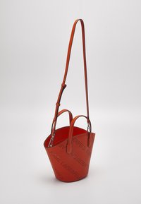 Sac seau en cuir rouge avec deux poignées et une bandoulière réglable, avec un motif de texte perforé sur la surface.