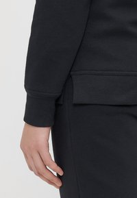 Sudadera oscura con puños y dobladillo acanalados, con pequeños detalles de ventilación lateral, hecha de una suave mezcla de algodón, con textura lisa.
