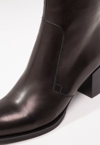 Bottine en cuir lisse marron foncé avec bout carré, talon bloc et discrètes surpiqûres le long du côté.