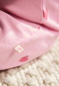 Sacco en tissu rose avec un motif en cœur subtil, surface texturée et une petite étiquette avec un détail en cœur rose.