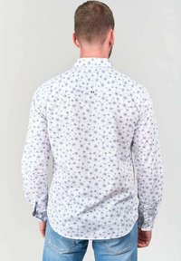 Witte blouse met lange mouwen en een blauw bloemenpatroon, met een button-down kraag en een klein logo detail nabij de schouder.