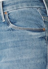 Primer plano de un bolsillo de pantalones vaqueros de denim azul claro con remaches de cobre visibles y costuras naranjas.