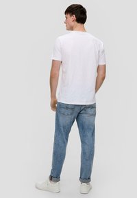 Biała bawełniana koszulka z krótkim rękawem, zestawiona z jasnoniebieskimi dżinsami. Białe trampki dopełniają stój, podkreślając swobodny styl.