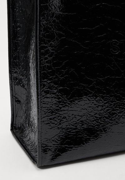 Black patent leather tote bag with a glossy, textured finish, featuring a rectangular shape and embossed branding on the surface.