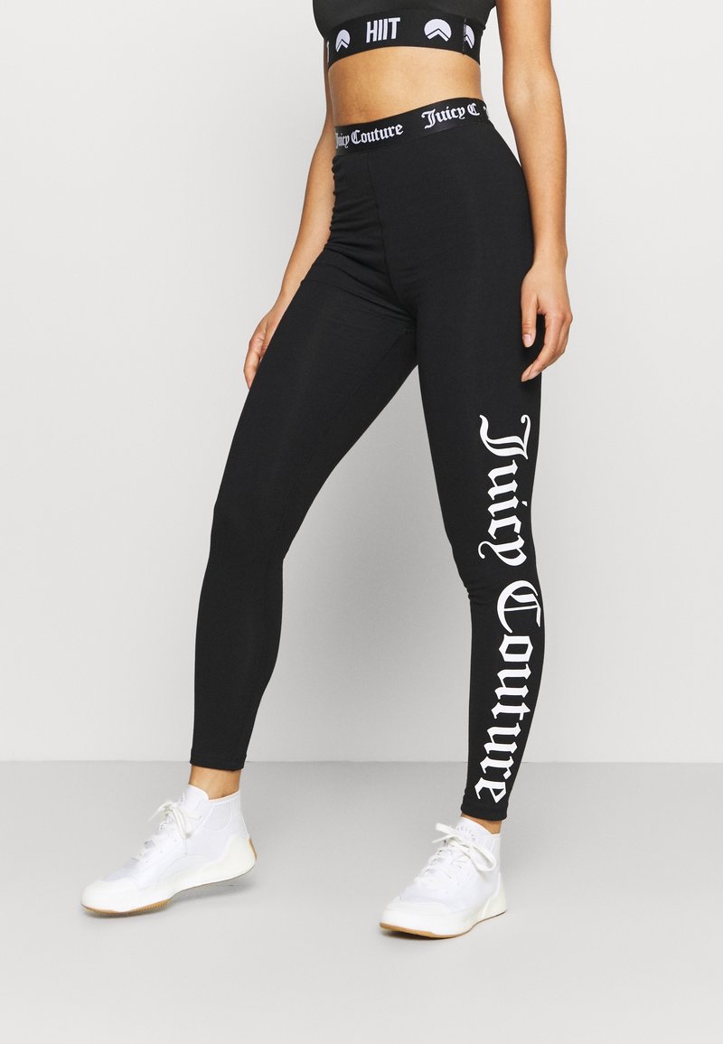 Leggings noirs avec une taille haute, arborant le logo "Juicy Couture" en blanc sur la jambe gauche. Faits d'un matériau extensible, conçus pour le confort.