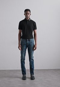 Must-haves: musta lühikeste varrukatega polo särk, sinised teksatooted ja mustad kingad. Modell seisab helesinise halli tausta vastu. Lihtne disain ja lõige.
