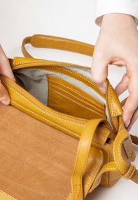 Tanfarbene Ledertasche mit gelben Lederakzenten. Das Innere ist mit gestreiftem Stoff und einer braunen Tasche mit roten Nähten ausgestattet.