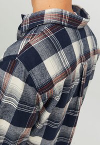 Blå och vit rutiga skjorta med orange detaljer, med en knäppningkrage och mjukt, texturerat tyg. Synliga sömmar och stygn detaljer.