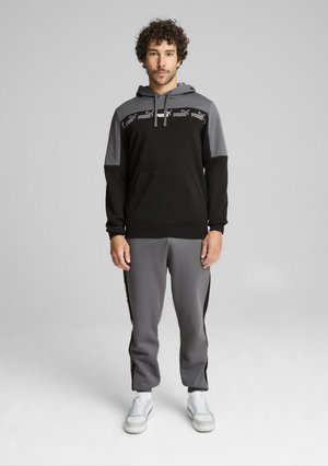 Czarny i szary dres z kapturem, zawierający bluzę z kieszenią kangurką i kolorystycznie zablokowanym wzorem. Dopasowane spodnie z bocznymi akcentami.