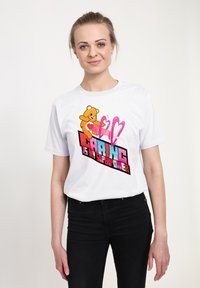 Camiseta blanca de manga corta con un oso de dibujo animado sosteniendo corazones y un texto en negrita que dice "Cuidar es mi superpoder" en rosa y azul.