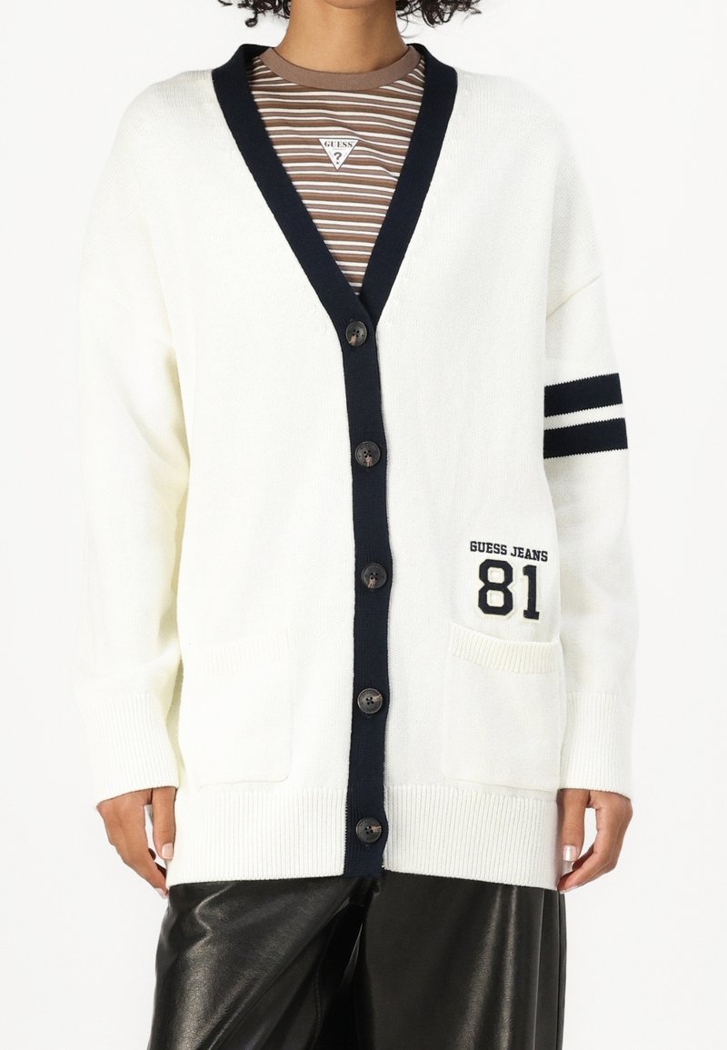 Cremefarbener Cardigan mit navyfarbigen Akzenten, V-Ausschnitt, Knopfverschluss, zwei Fronttaschen und einem sportlichen Streifenmuster am Ärmel.