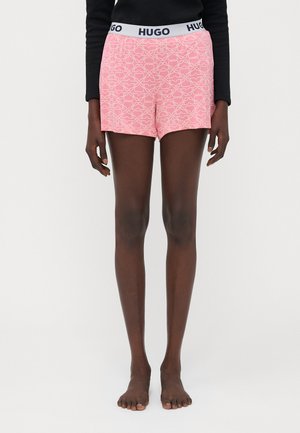 Pink shorts with a geometric white pattern, elastic waistband labeled "HUGO." Made of lightweight fabric, featuring a relaxed fit.