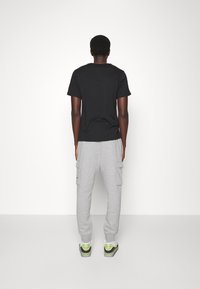 Svart t-shirt med kort ärm som är kombinerad med grå cargojoggers med sidofickor. Skorna är vita med gröna accenter.