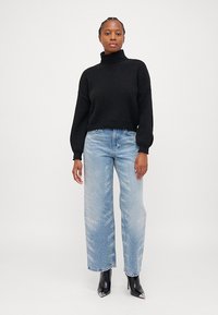 Maglione a collo alto nero in maglia, abbinato a jeans a gamba larga azzurri chiari con leggere macchie, e stivaletti neri a punta.