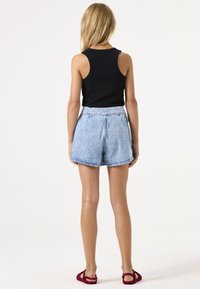 Zwarte geribbelde tanktop gecombineerd met high-waisted lichtblauwe denim shorts. De shorts hebben een relaxte pasvorm en een franjeszoom. Rode sandalen maken de look compleet.