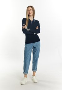 Polo a maniche lunghe a coste di colore blu navy con strisce bianche sui polsini, abbinato a jeans in denim azzurro arrotolati e sneakers bianche.