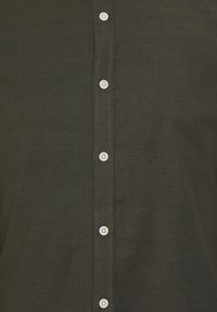 Camisa de algodón negra con cierre frontal de botones blancos. Textura suave y detalle de costura neat a lo largo de la lengüeta.