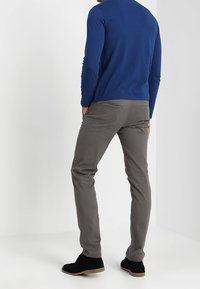 Grå slim-fit byxor med bakfickor, ihop med en blå långärmad skjorta och svarta ankelstövlar, mot en neutral bakgrund.