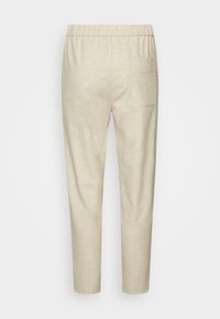 Pantalons beiges en lin avec une taille élastique, jambes fuselées et une poche arrière plaquée unique. Texture lisse et design minimaliste.