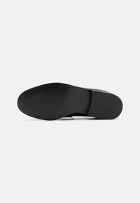 Suela de zapatos de cuero negro con un patrón de agarre texturizado, ligera curvatura y marca en relieve. Acabado suave con color uniforme.