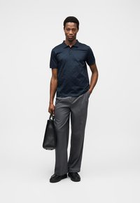 Ναυτικό μπλουζάκι πόλο, γκρι παντελόνια, μαύρα παπούτσια και μαύρη τσάντα χειρός. Λείο ύφασμα, άνετη εφαρμογή και κλασικός σχεδιασμός γιακά.