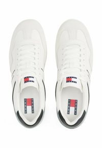 Zapatillas blancas con un diseño de cuero suave, punta redonda, cierre de cordones, un detalle negro en el talón y una etiqueta con el logo en la lengüeta.