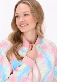 Giacca bomber colorata con un motivo a spirale nei toni del rosa pastello, blu e giallo, con collo e polsini a coste rosa.