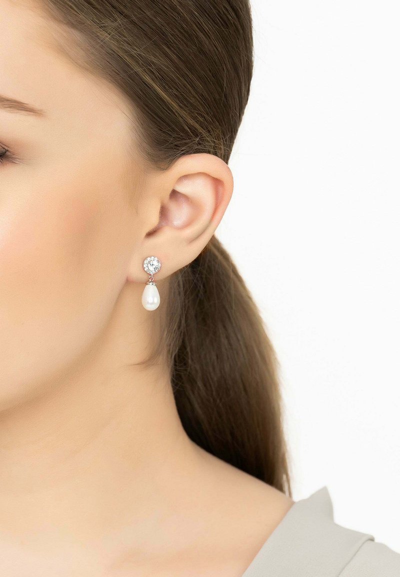 Csepp alakú fülbevalók ezüst színű kerettel, melyek fehér gyöngy csepp alatt egy kerek kristály díszítéssel rendelkeznek, és a fülcimpától lógnak.