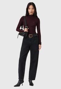 Bordeaux roter Langarmoberteil, hoher Kragen, schwarze hochgeschnittene Jeans, schwarze Absatzstiefel, schwarze Schultertasche mit goldenen Akzenten, glattes Material, lässige Passform.