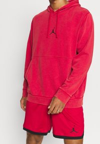 Haut en polaire rouge avec une poche kangourou et le logo Jordan noir. Associé à un short rouge avec un accent noir et un logo.