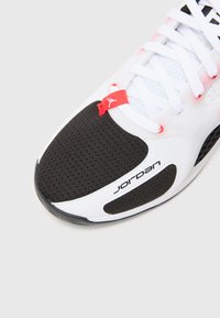White and black sneaker with a perforated upper, red accent, and Jordan branding. Features a rounded toe and textured sole.