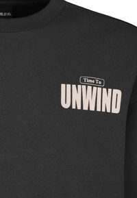 Zwarte sweatshirt gemaakt van zacht materiaal met een ronde hals. De voorkant toont de tekst "Time To UNWIND" in crèmekleurige letters.